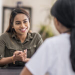 A stressed-out woman is chatting with her mental health counselor. She is explaining her problems. She is staying positive with a smile.
