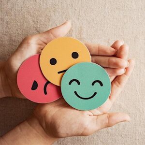 Hands holding symbols of various emotions: happy, neutral, sad